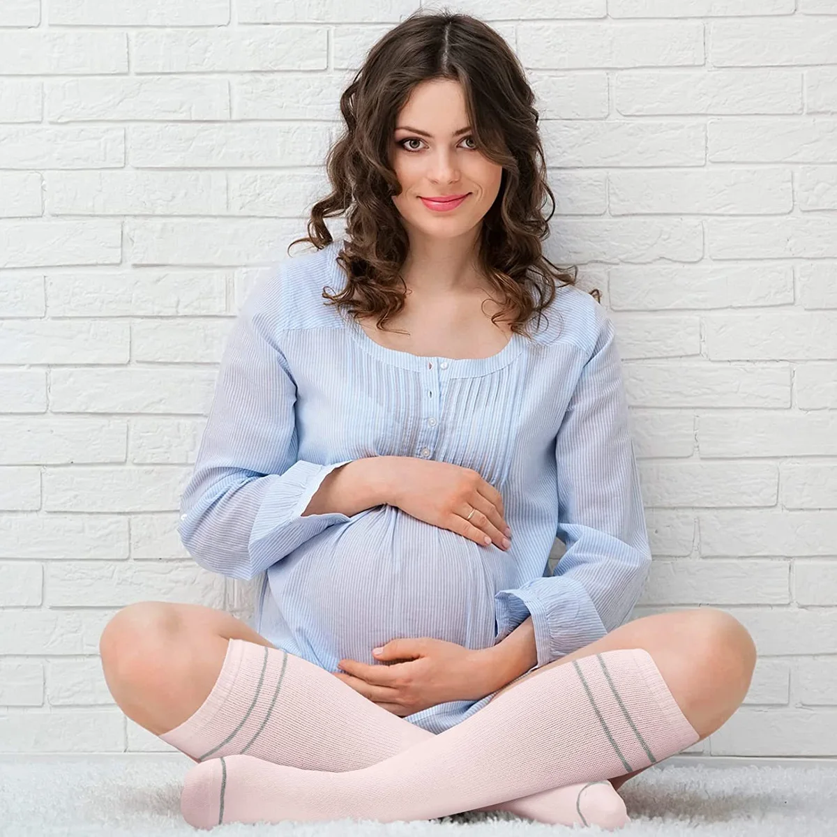Femme enceinte assise en tailleur portant des chaussettes hautes rose poudré